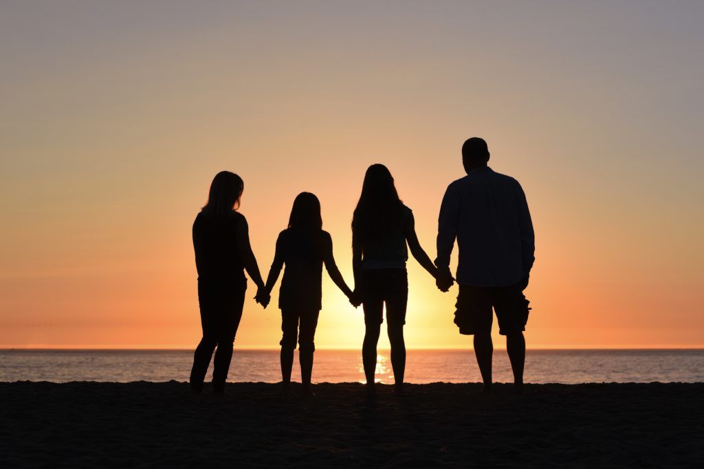 the silhouette of a parenting coach sessionof four holding hands looking at the sunset at the beach