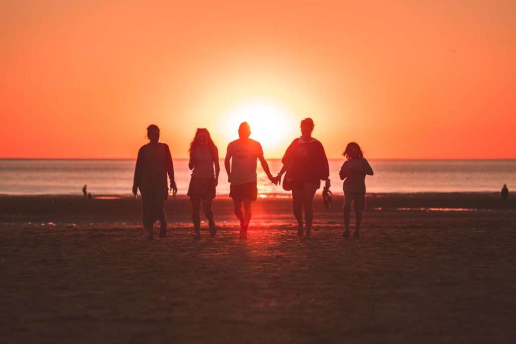 Silhouetted family of five walking at a beach at sunset.