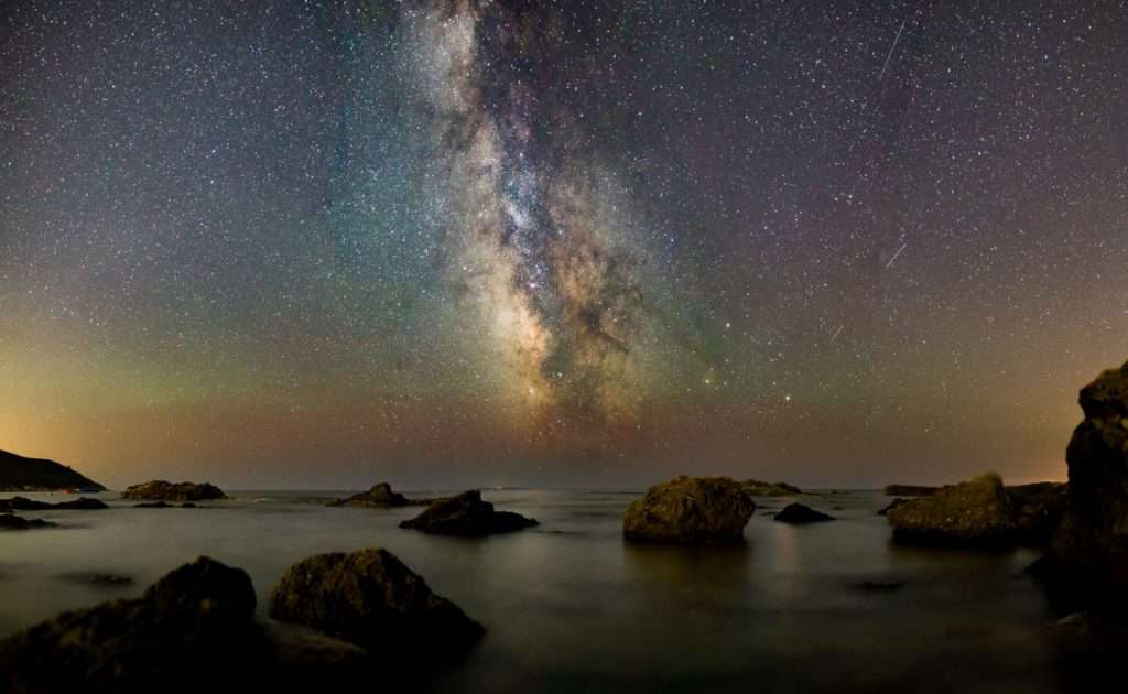 galaxy of stars in the night sky at a rocky coastline.