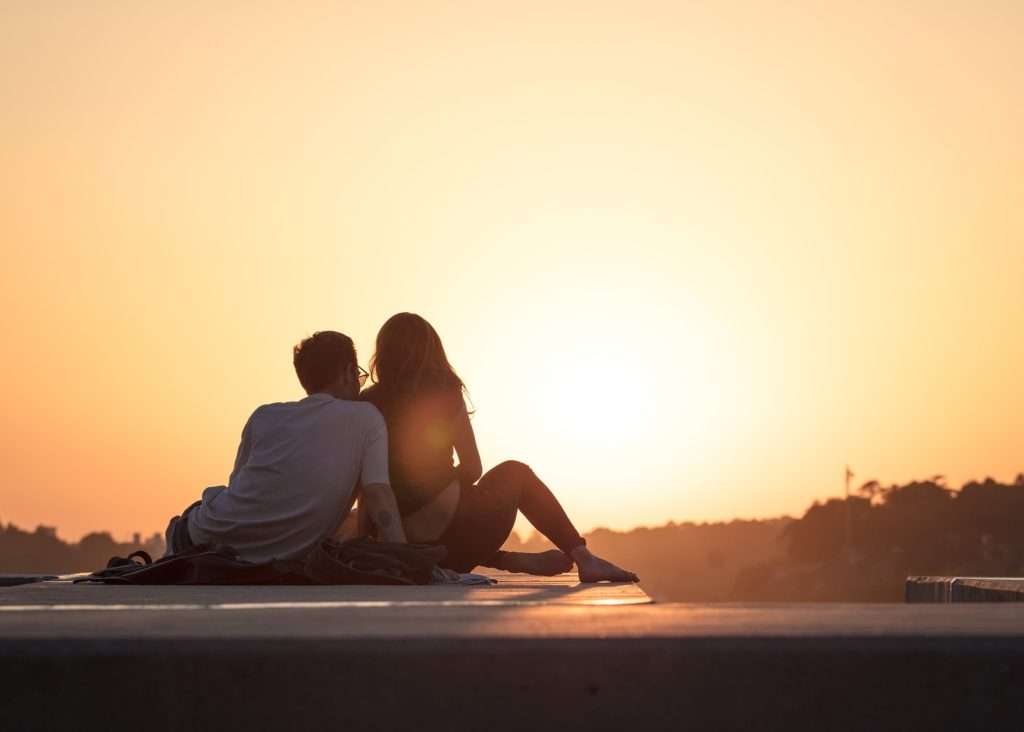 young couple sitting on a blanket on a dock at sunset with a soft amber sky