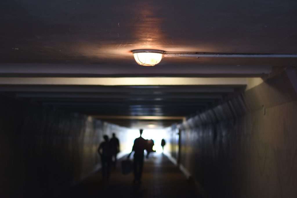 a ceiling light is in focus and the blurred view of a tunnel with people walking in the distance.