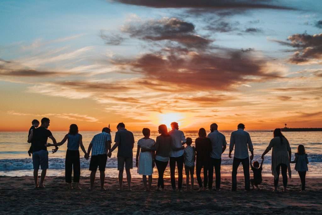 A large family of 15 standing toward the sunset at the beach in soft red and amber light